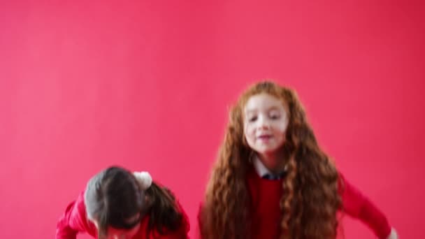 两名小学女生在红色工作室的背景下 从屏幕底部跳到一个空的框架里 笑着看着相机 慢镜头 — 图库视频影像