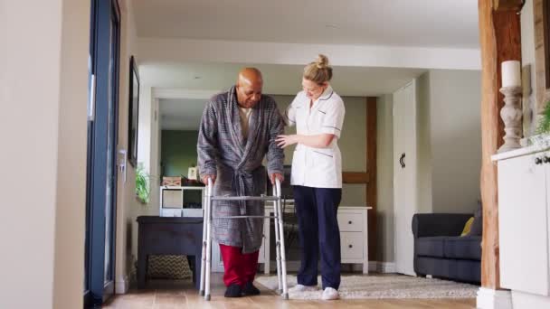 ウォーキングフレームを使用してガウンを身に着けているシニア男は女性介護労働者によって助けられて スローモーションで撮影 — ストック動画