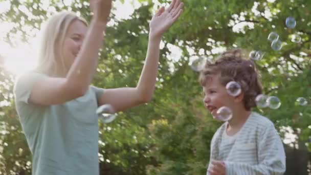 母亲带着儿子在花园追逐和爆裂的泡沫中玩乐 慢镜头拍摄 — 图库视频影像