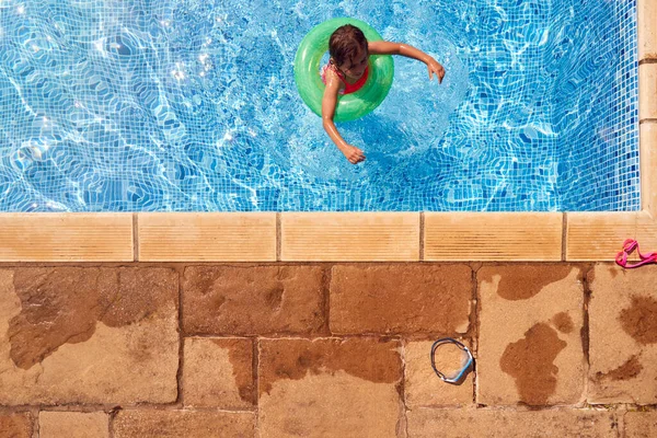夏休みに水泳プールでインフレータブルリングで泳ぐことを学ぶ女の子のオーバーヘッドビュー — ストック写真