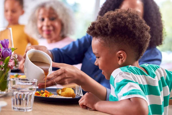 多世代家族として息子の食事に重力を注ぐ母は自宅でテーブルの周りに座る — ストック写真