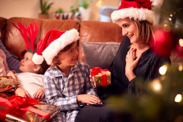 Son Giving Mother Gift As Family Sitting On Sofa At Home Opening Christmas Presents