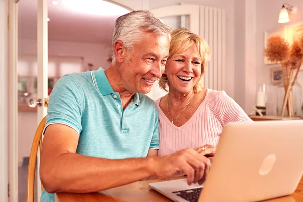 年长的退休夫妇坐在沙发上在家购物或在笔记本电脑上预订假期 — 图库照片