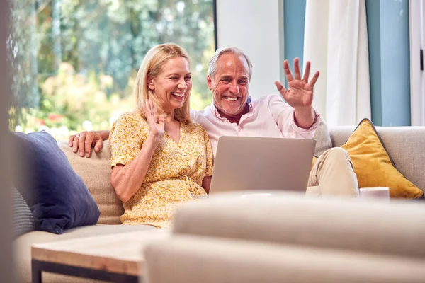 老人夫婦が自宅でソファに座っているラップトップでビデオ通話をする — ストック写真