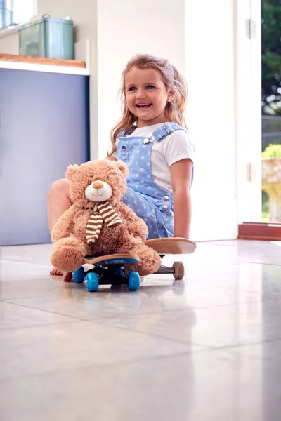在家里和泰迪熊一起玩滑板游戏的小女孩笑着 — 图库照片
