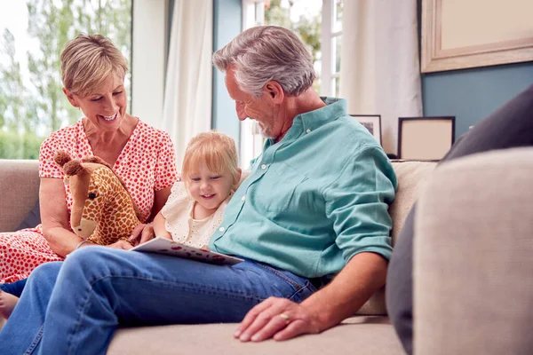 Großeltern Sitzen Mit Enkelin Hause Auf Sofa Und Lesen Gemeinsam — Stockfoto