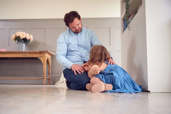 父亲抱着玩具熊坐在地板上的不快乐女儿 — 图库照片