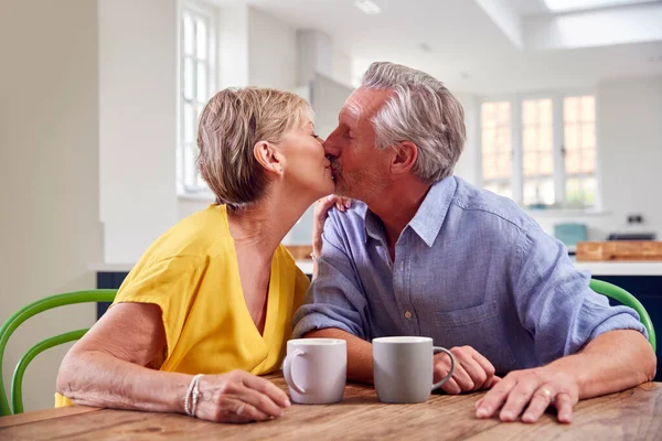 Kissing Retired Couple Sitting Table Home Having Morning Coffee Together — Stock Photo, Image