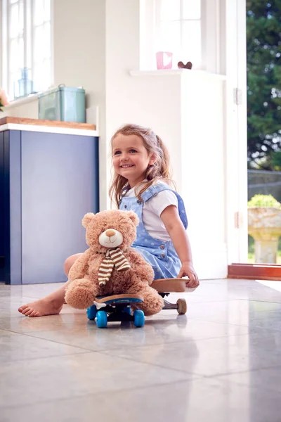 Leende Ung Flicka Spelar Spel Sitter Skateboard Med Nallebjörn Hemma — Stockfoto