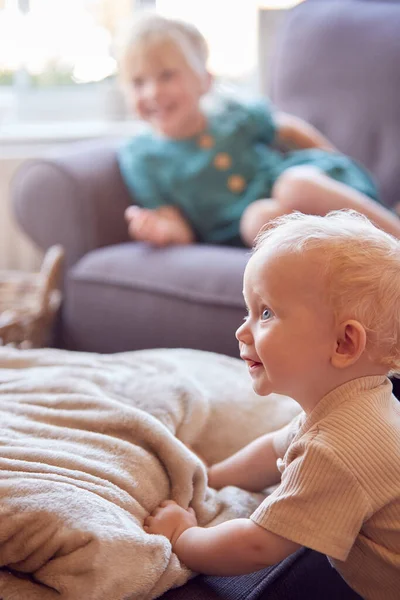 幼い女の子が家でソファに座ってテレビを見ている赤ちゃんの弟が前景で遊ぶ — ストック写真