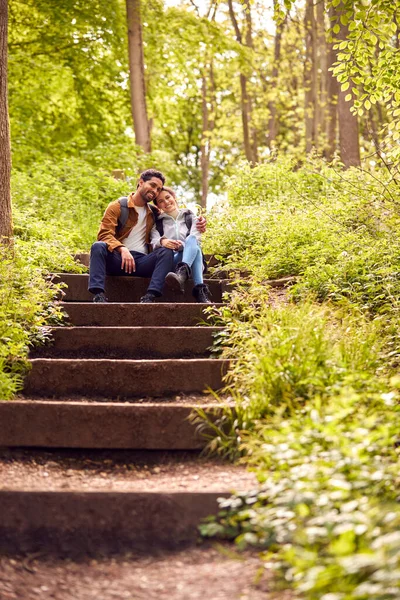 バックパック付きのハイキングカップルが田舎の木を通って階段に座って一緒に — ストック写真
