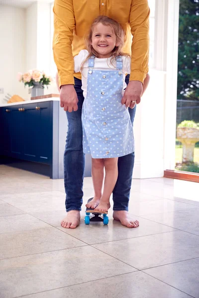 父亲帮助女儿在家中滑板上保持平衡 — 图库照片