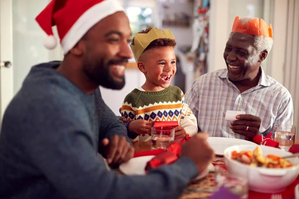 Flergenerationsfamilj Pappershattar Läsa Jul Cracker Skämt Innan Äter Mat Tillsammans — Stockfoto