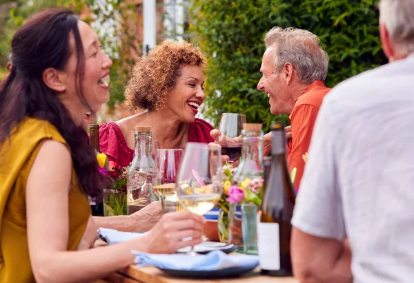 在家庭花园举行的夏季晚宴上 一群成熟的朋友围坐在桌旁聊天 — 图库照片