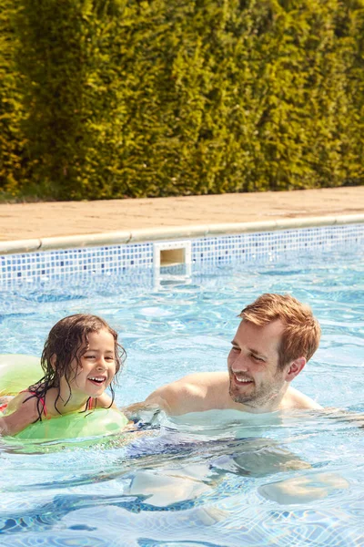 父亲在暑期游泳池教女儿带着充气环游泳 — 图库照片