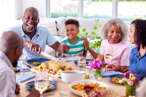 多世代家族として彫刻祖父は自宅でテーブルの周りに座って食事を楽しむ — ストック写真