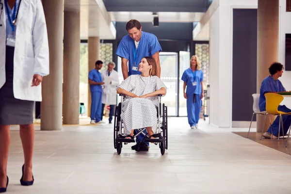 男护士穿着洗涤器推送女病人通过医院大楼 — 图库照片