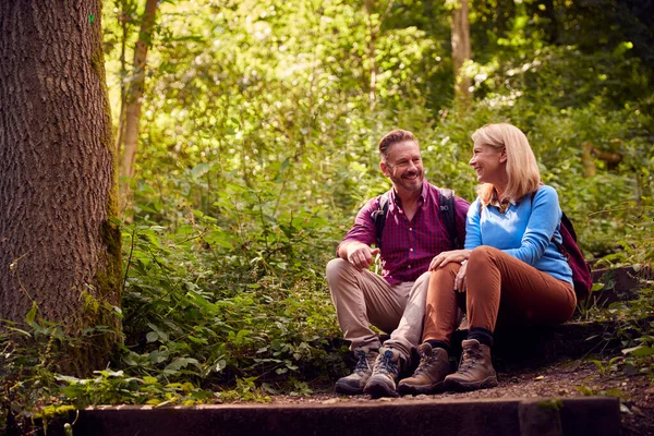 Mature Couple In Countryside Hiking Along Path Through Forest Sit And Take A Break Together