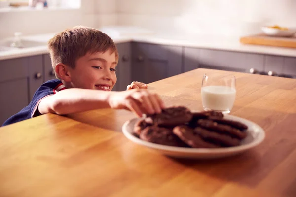 カウンターの上のプレートからクッキーを取るために到達キッチンで自宅で男の子 — ストック写真