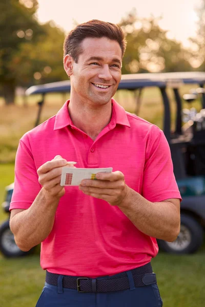 スコアカードとゴルフコースでバギーで立つ笑顔の男性ゴルファーの肖像 — ストック写真