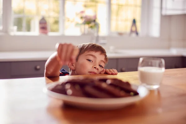 カウンターの上のプレートからクッキーを取るために到達キッチンで自宅で男の子 — ストック写真