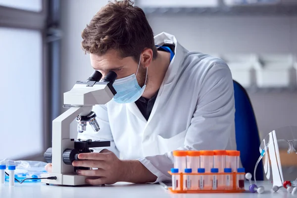 顕微鏡で血液サンプルを分析するPpeを身に着けている男性研究室の労働者 — ストック写真