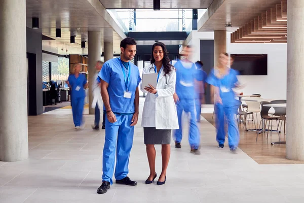 白衣を着た男性と女性医師とデジタルタブレットを見てこすります忙しい病院 — ストック写真