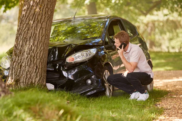 車の横にいる男が事故被害を調査し 緊急サービスを呼び出す木に衝突 — ストック写真
