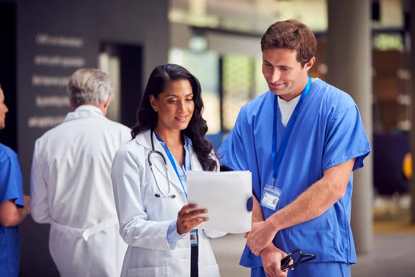 病院で正式な会議を持っているデジタルタブレット付きホワイトコートとスクラブの2人の医療スタッフ — ストック写真