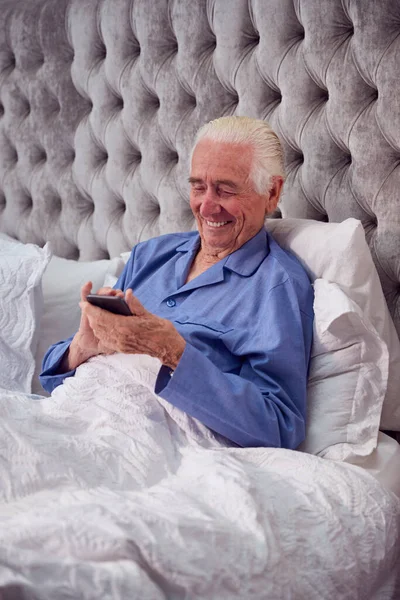 Smiling Senior Man Home Wearing Pyjamas Bed Using Mobile Phone —  Fotos de Stock