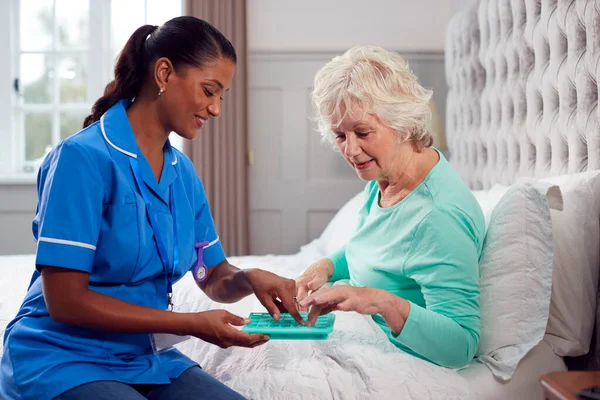 Працівник Догляду Жінкою Уніформі Допомагає Старшій Жінці Вдома Ліжку Ліками — стокове фото
