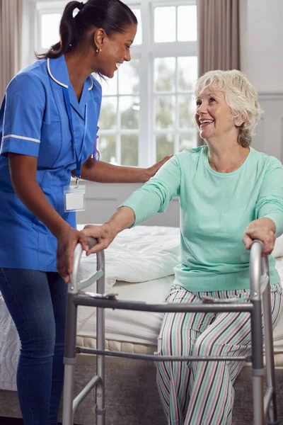 穿着制服的女性护理人员帮助老年妇女从床上走出来 在家使用步行架 — 图库照片