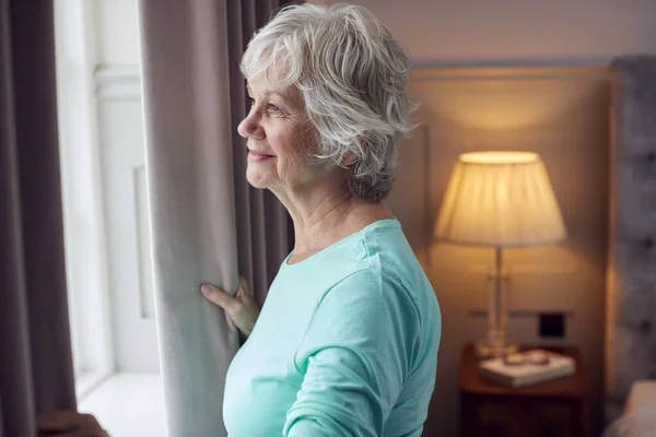 Smiling Senior Woman Home Wearing Pyjamas Opening Bedroom Curtains Looking — Stock fotografie