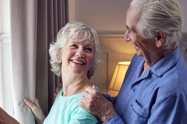 Smiling Senior Couple Home Wearing Pyjamas Opening Bedroom Curtains Looking — ストック写真