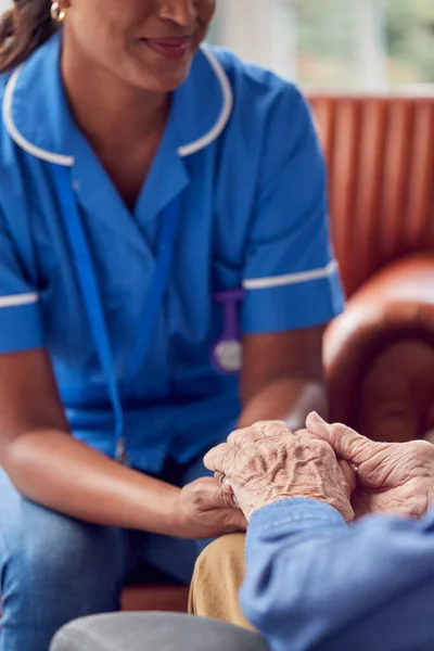 介護ホームラウンジに座っているシニア男性の手をつなぐ制服介護士のクローズアップ — ストック写真