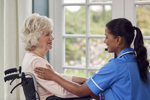 穿着制服的女性护理人员与坐在养老院客厅轮椅上的老年妇女交谈 — 图库照片