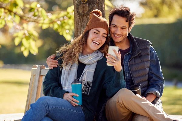 Smiling Couple Sitting Bench Autumn Park Using Mobile Phone — Stock Fotó