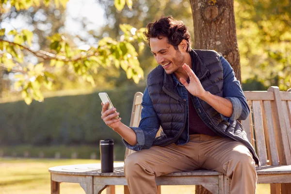 Homme Souriant Assis Sur Banc Faisant Appel Vidéo Dans Parc — Photo