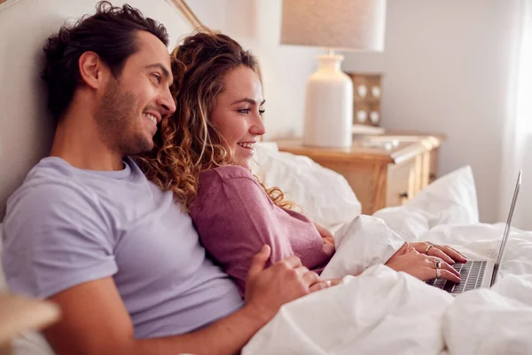 自宅で寝そべっているパジャマ姿のカップルがノートパソコンを見ながら一緒に — ストック写真