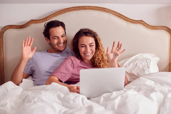 Loving Couple Wearing Pyjamas Lying Bed Home Making Video Call — Stok fotoğraf