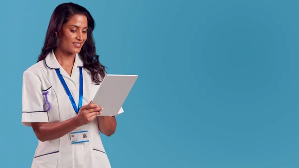 Smiling Female Mature Nurse Wearing Uniform Digital Tablet Front Blue — Zdjęcie stockowe