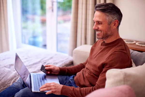 Dojrzały Mężczyzna Domu Siedzi Kanapie Laptopem Płacąc Zakupy Online Karty — Zdjęcie stockowe