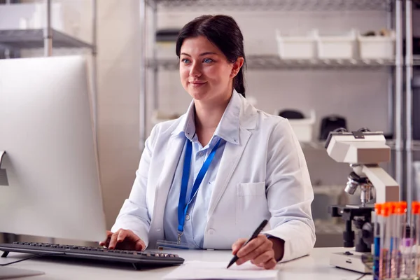 穿着Ppe面罩的女性实验室工作人员在计算机上记录血液检测结果 — 图库照片