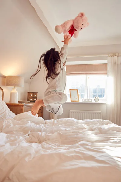 活泼的年轻姑娘精力充沛地在床上蹦蹦跳跳 带着柔软的玩具 — 图库照片