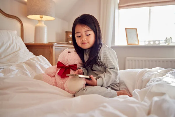 Menina Jovem Sentada Cama Com Telefone Móvel Vestindo Pijama Casa — Fotografia de Stock