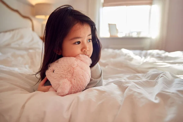 若いです女の子座っていますベッドの上に身に着けていますパジャマ ホームカッディングソフトおもちゃ — ストック写真