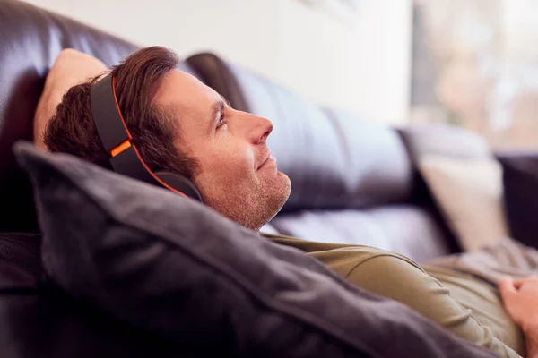 Man Bär Trådlösa Hörlurar Lyssna Musik Som Ligger Soffan Hemma — Stockfoto