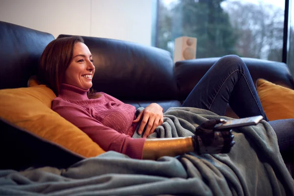 義肢を持つ女性と自宅でソファの上でリラックステレビを見て — ストック写真