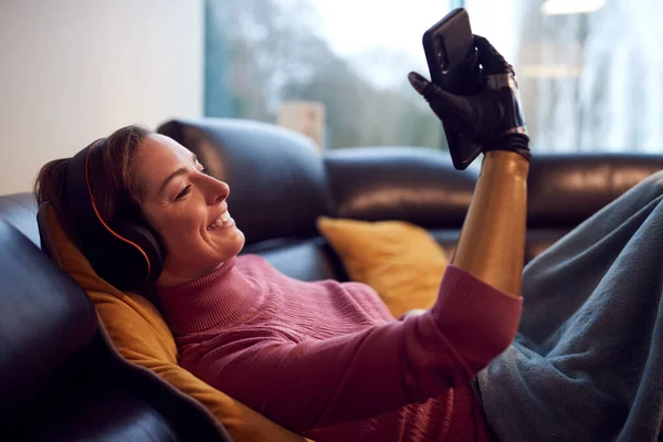 Kobieta Protetycznym Ramieniem Słuchawkach Bezprzewodowych Słuchanie Muzyki Telefonie Komórkowym Kanapie — Zdjęcie stockowe
