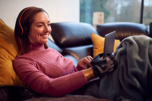 Woman Prosthetic Arm Wearing Wireless Headphones Watching Movie Laptop Sofa — стоковое фото